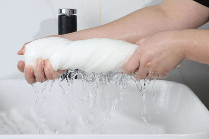 Person wringing out a soft, absorbent white towel over a sink, demonstrating its quick-drying quality.