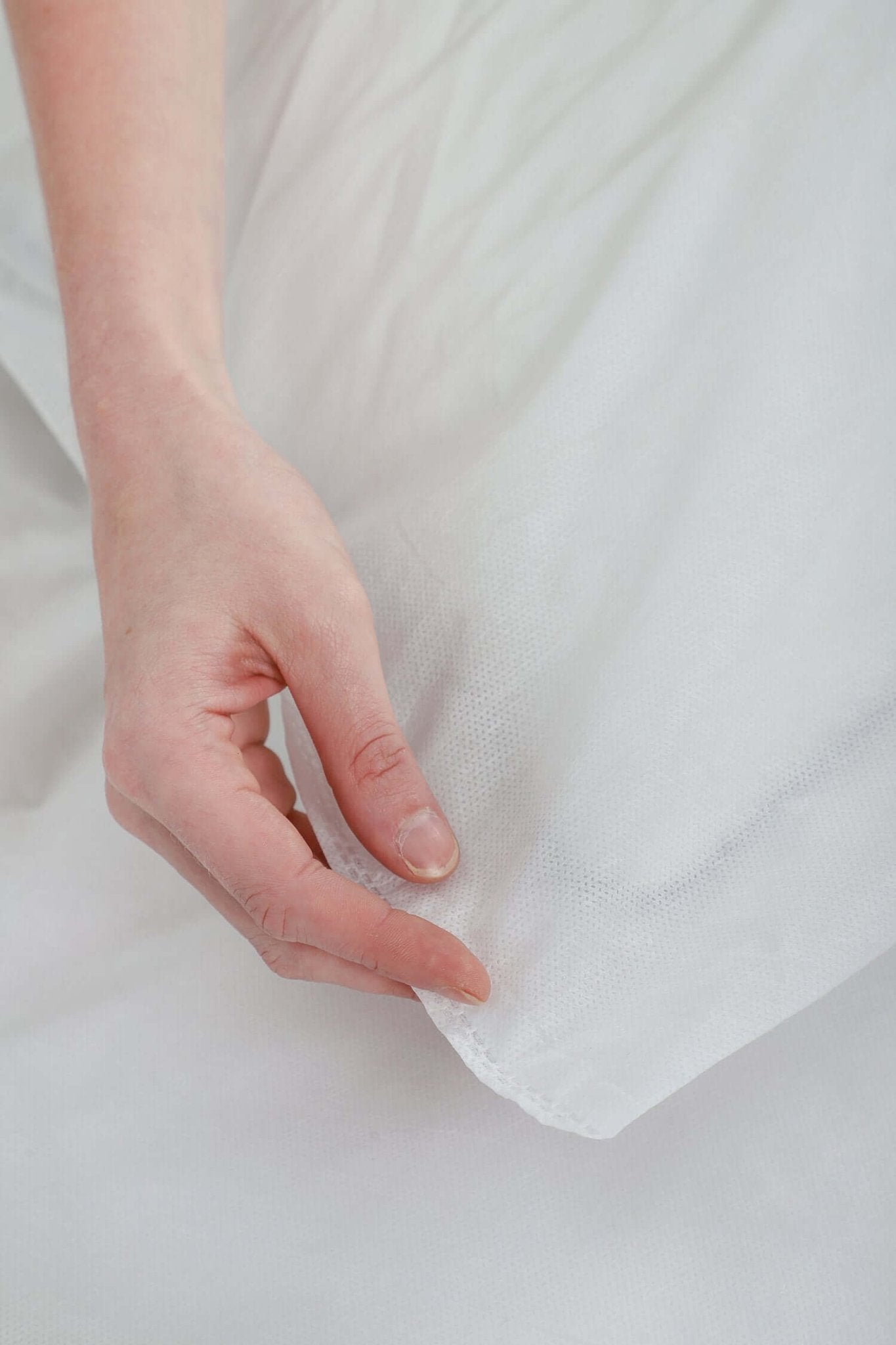 Close-up of a hand holding soft, breathable disposable bed cover made from high-quality non-woven fabric.