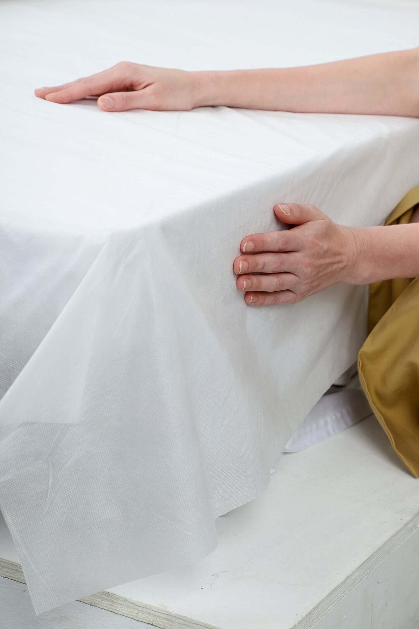 Close-up of a hand adjusting a white disposable bed cover on a mattress, showcasing its smooth texture.